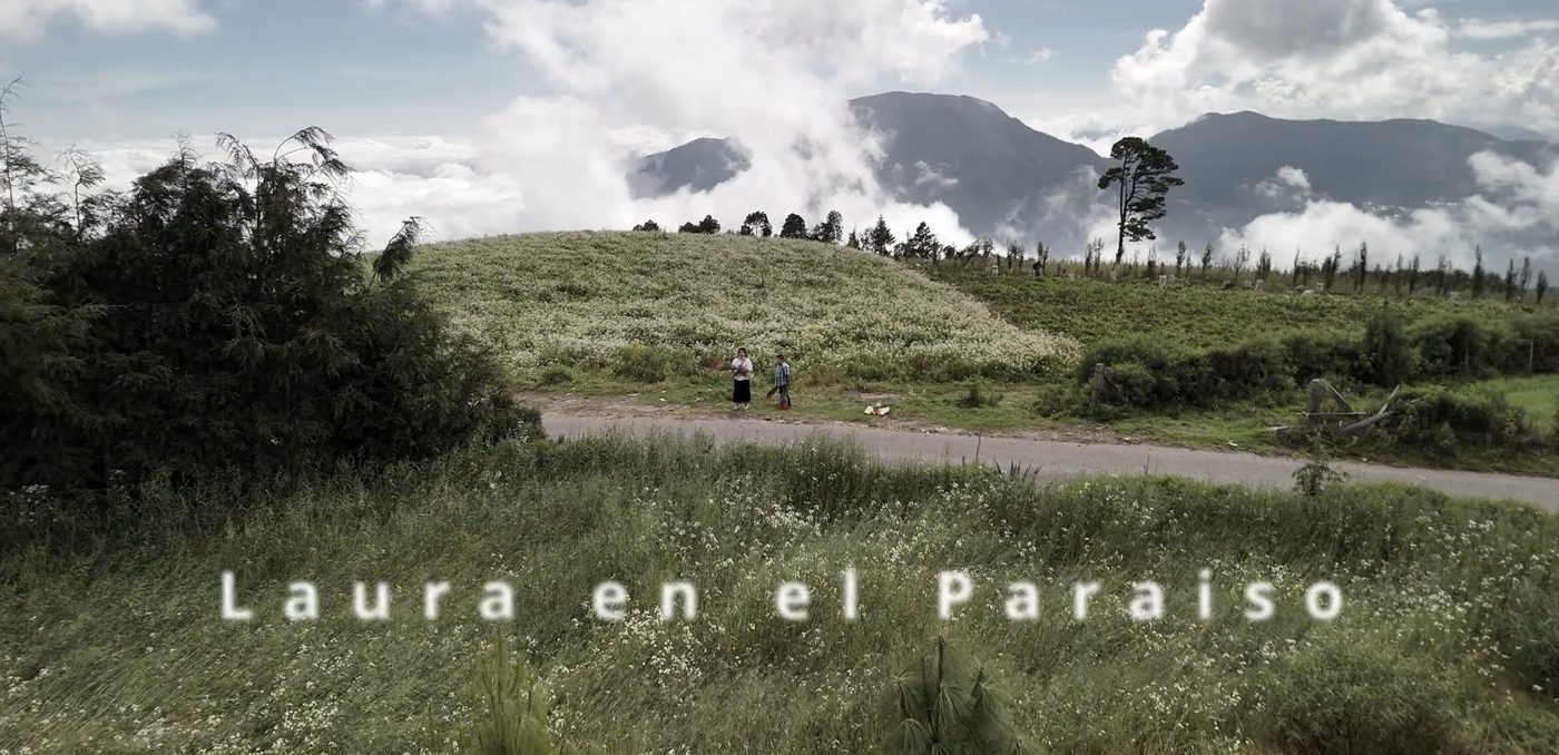 Fotograma del teaser de Laura en el paraíso: dos figuras en un camino entre montañas y nubes